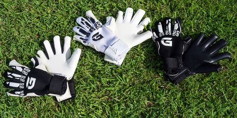 three sets of goalkeeping gloves laying flat on grass